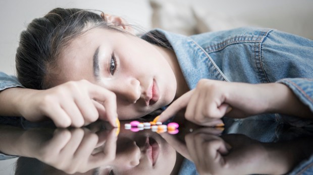 Picture of teenage girl looks sad while counting drugs on the table at home